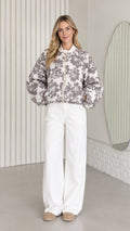 Front view of model wearing charcoal floral zip-up bomber jacket with white trousers