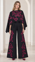 Front view of model wearing black embroidered cape sleeve wide leg jumpsuit
