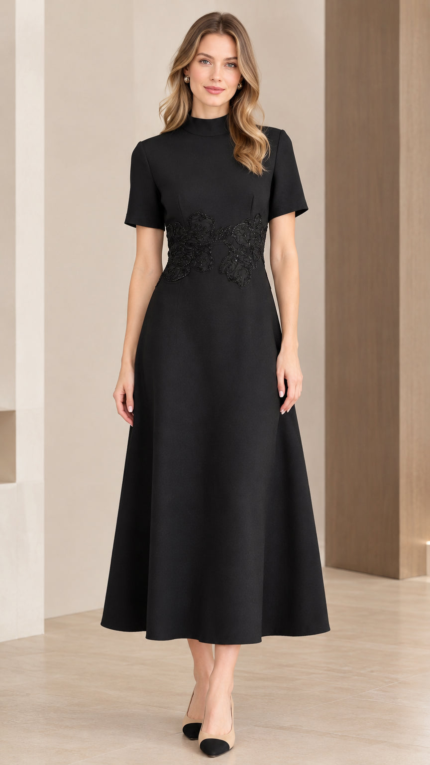 Front view of woman wearing elegant black mock neck A-line midi dress with beaded waist appliqué