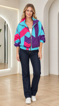Front view of woman wearing turquoise geometric colorblock zip-up windbreaker with dark jeans