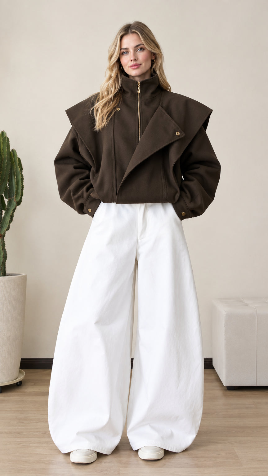 Front full view of woman wearing dark brown asymmetrical flap zip-up jacket with wide white trousers