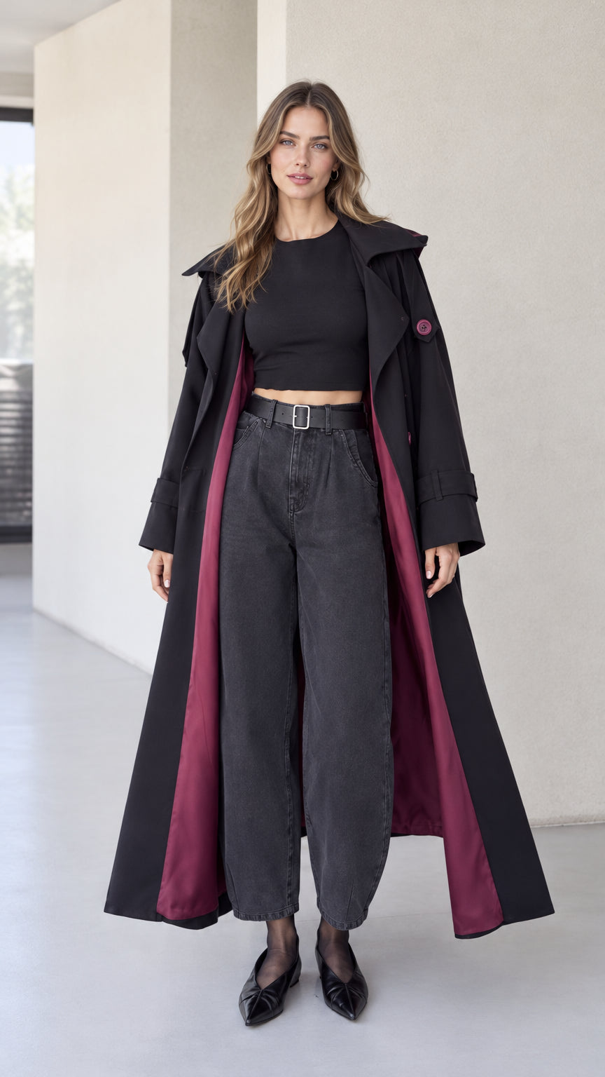 Full front view of model wearing black hooded maxi trench coat with contrast wine red lining
