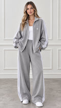 Front view of woman wearing grey two-piece tracksuit with white stripes and wide-leg pants