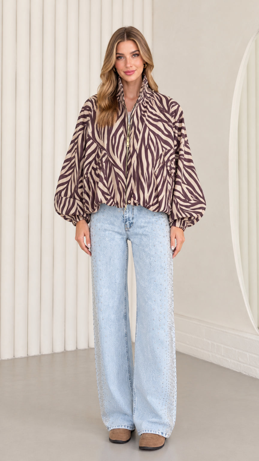 Front view of model wearing mocha brown zebra print balloon sleeve zip-up jacket with light-wash wide-leg jeans