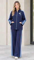 Front full-length view of woman wearing navy blue two-piece tracksuit with side stripes and floral chest appliqué
