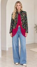 Front full-length view of model wearing black and magenta floral jacquard fringe jacket with wide-leg jeans