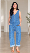 Front full-length view of model wearing relaxed denim blue sleeveless V-neck jumpsuit with cuffed hems