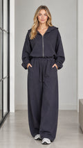 Front full-length view of woman wearing a charcoal zip-front hooded wide-leg jumpsuit