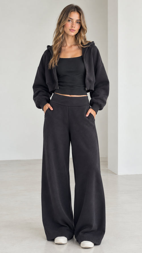 Full front view of model wearing the black 3-piece cropped hoodie, tank, and wide-leg sweatpants set