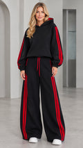 Front view of woman wearing black 2-piece hoodie and wide leg tracksuit set with red stripes