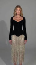 Front view of model wearing black velvet corset long sleeve fringe midi dress