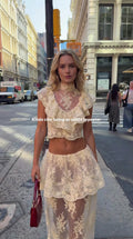 Full front view of model wearing cream floral lace ruffled crop top and tiered maxi skirt set on city street