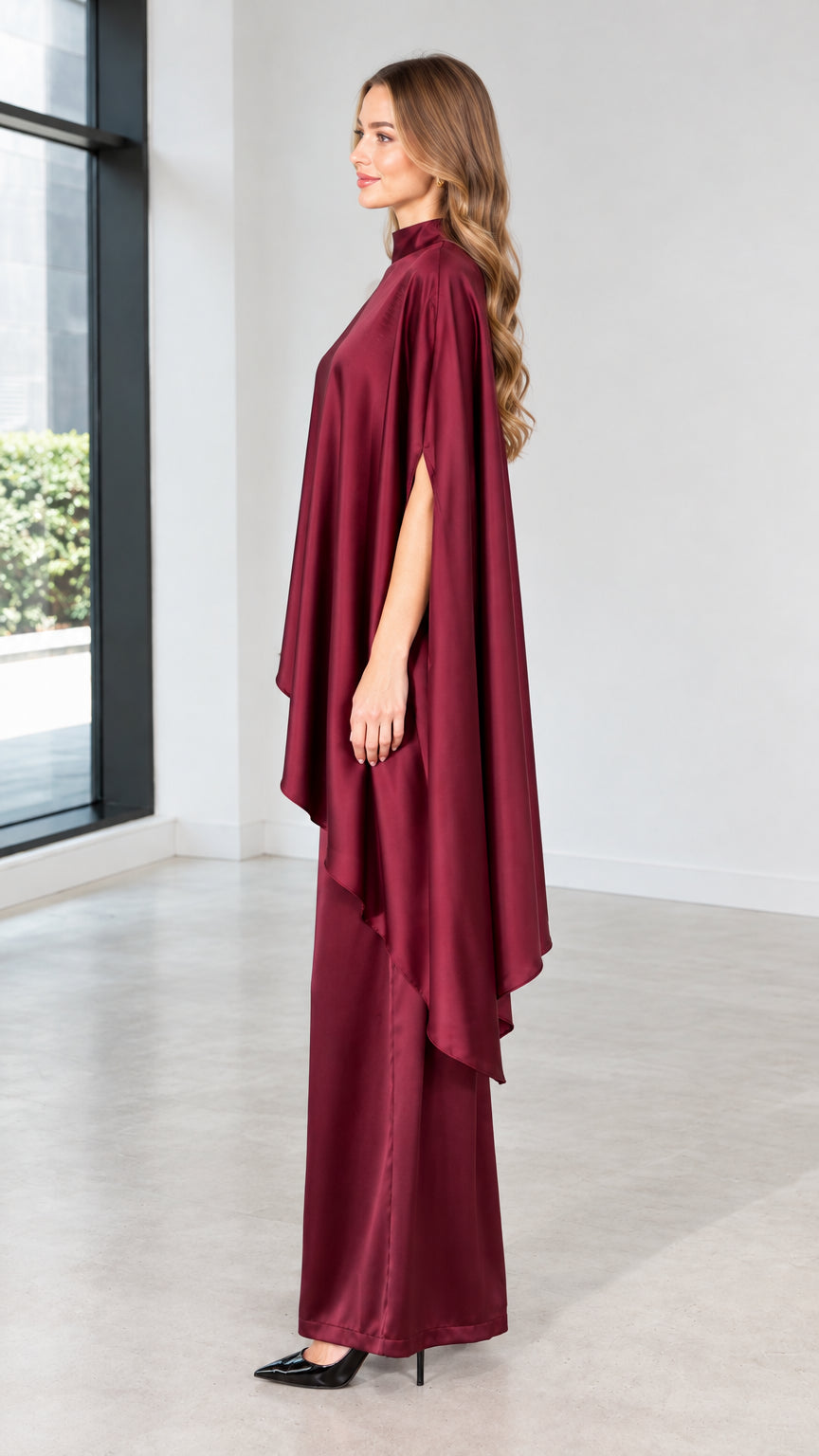 Side view of model wearing burgundy satin high-neck capelet blouse and flowing trousers