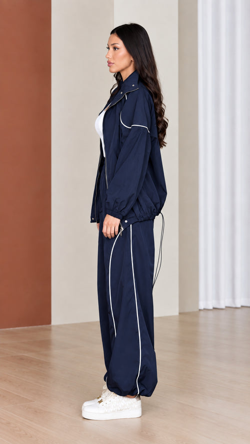 Side profile of woman wearing navy windbreaker jacket and matching parachute pants