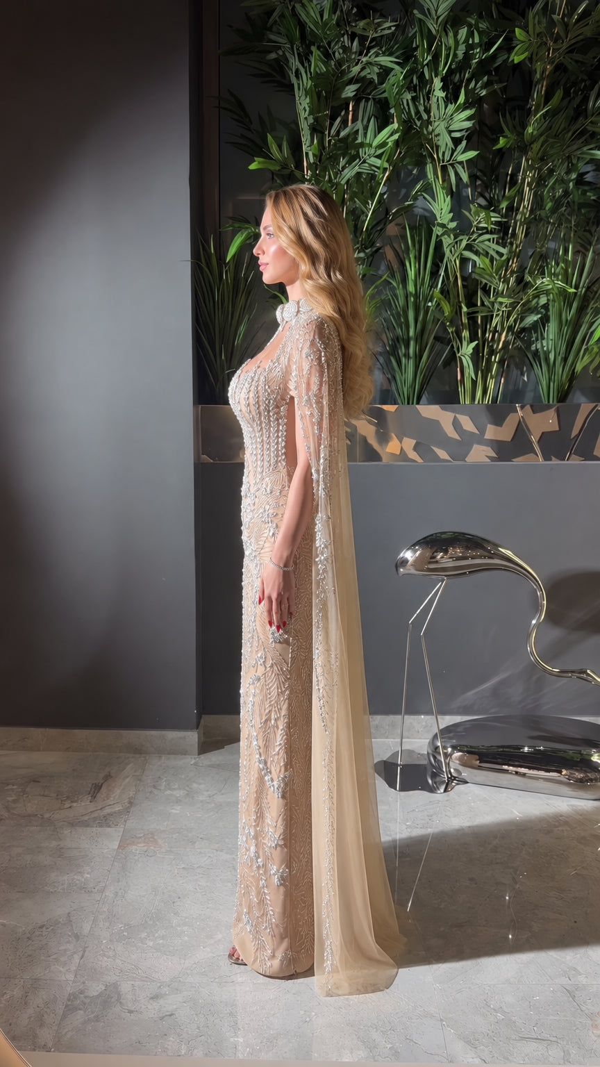 Side profile of champagne beaded formal gown showing silhouette and cape length