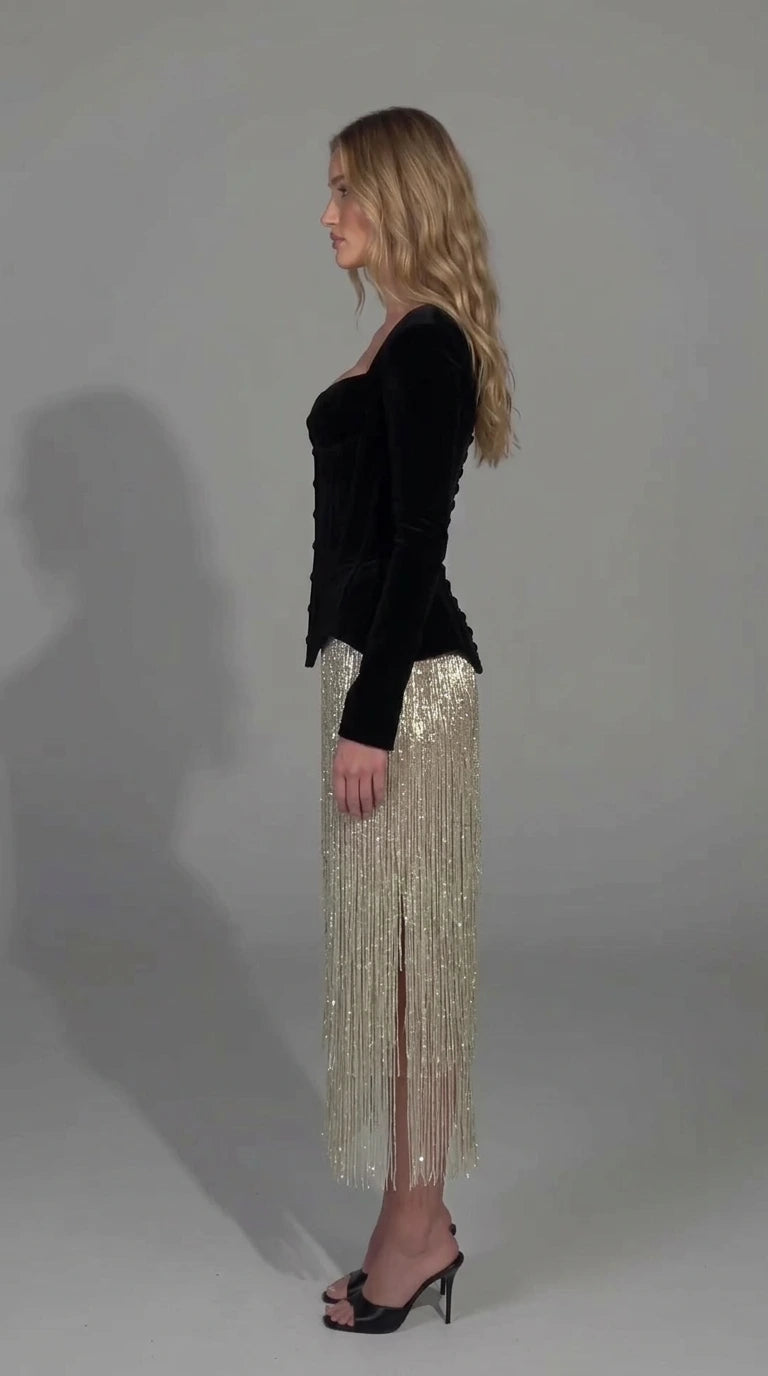 Side angle view of model in black velvet corset fringe midi dress