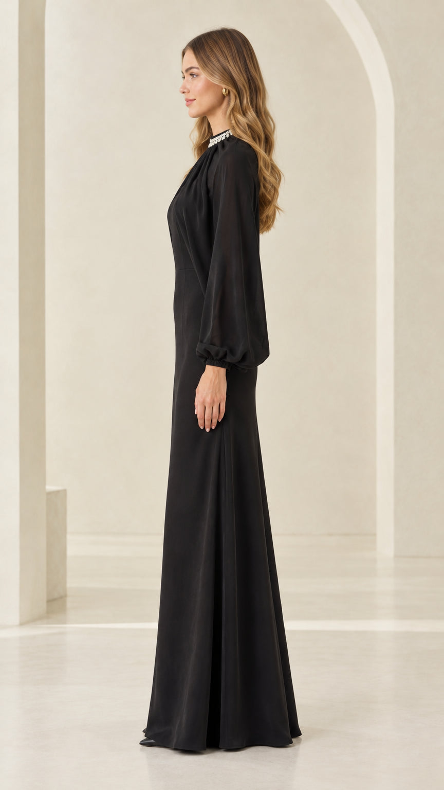 Side profile view of woman modeling black long sleeve cape formal gown