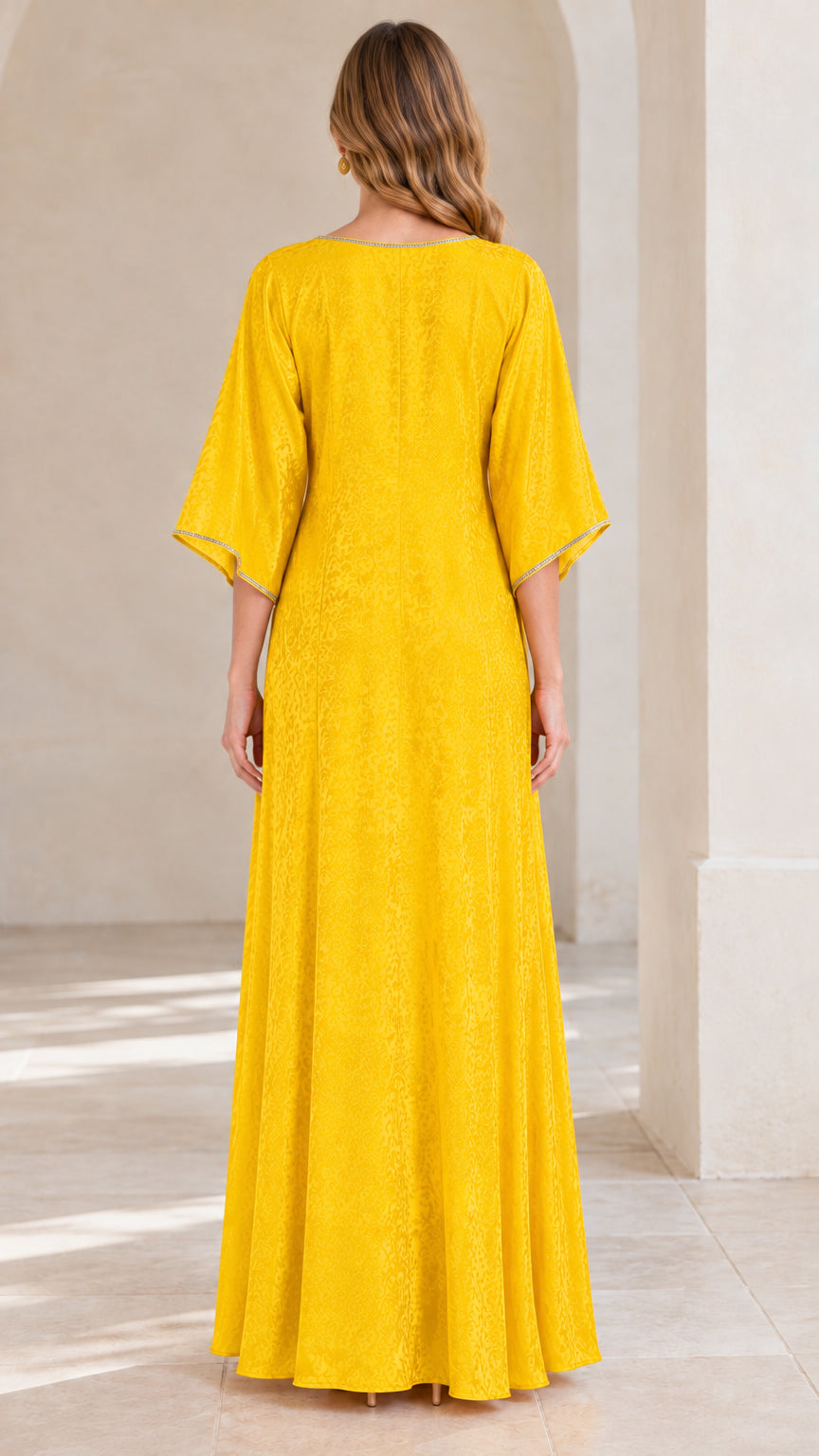 Back view of woman in flowing yellow jacquard kaftan maxi dress