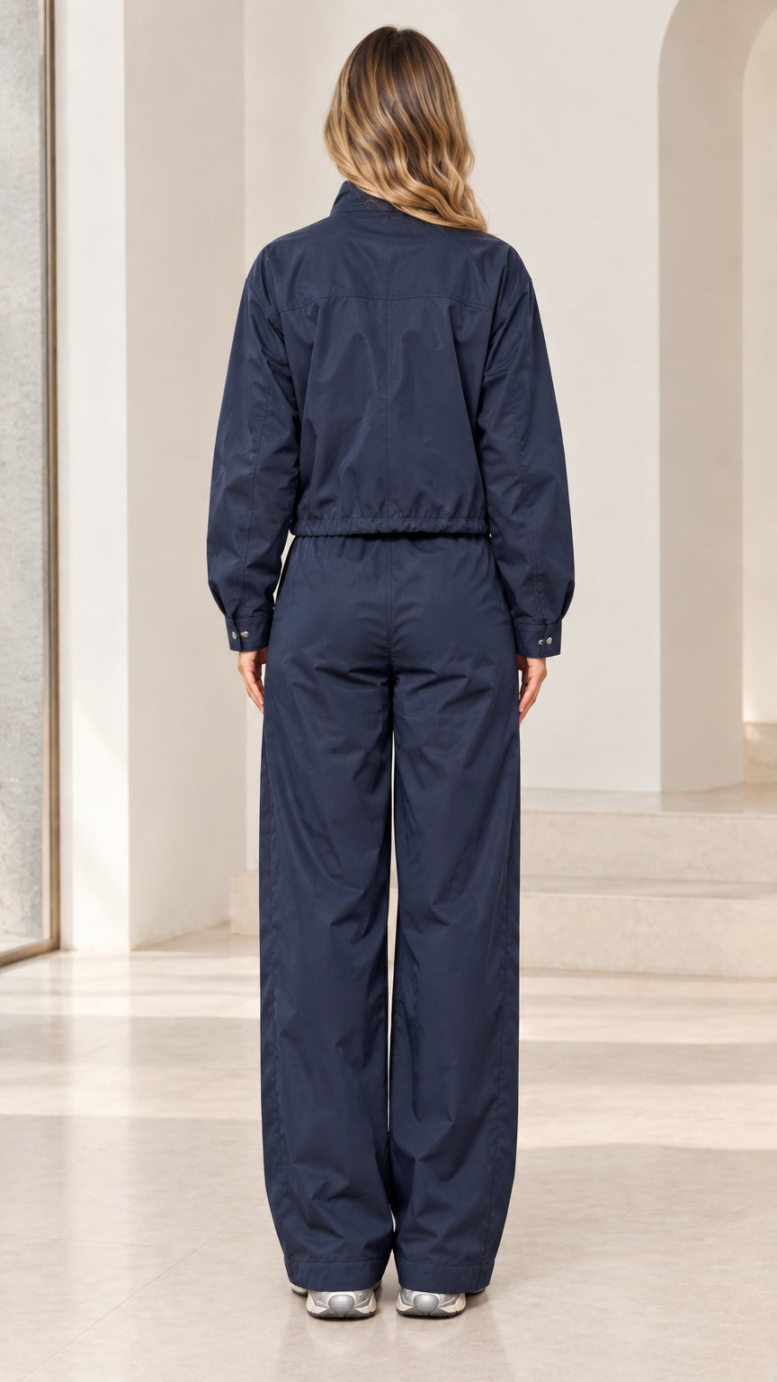 Back full-length view of woman wearing navy blue track jacket and wide-leg pants