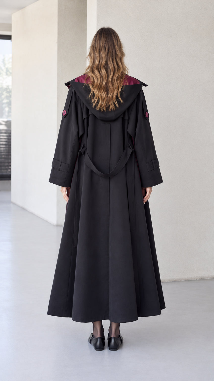 Back view of women's black maxi trench coat showing attached hood and back belt detail