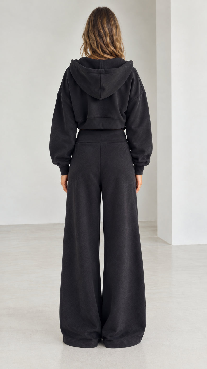 Back view of model wearing the black cropped zip hoodie and wide-leg sweatpants