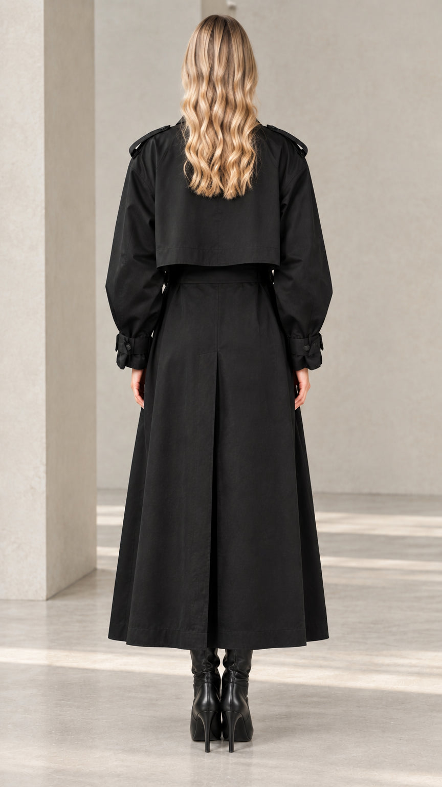 Back view of women's black maxi trench coat highlighting storm flap and inverted pleat