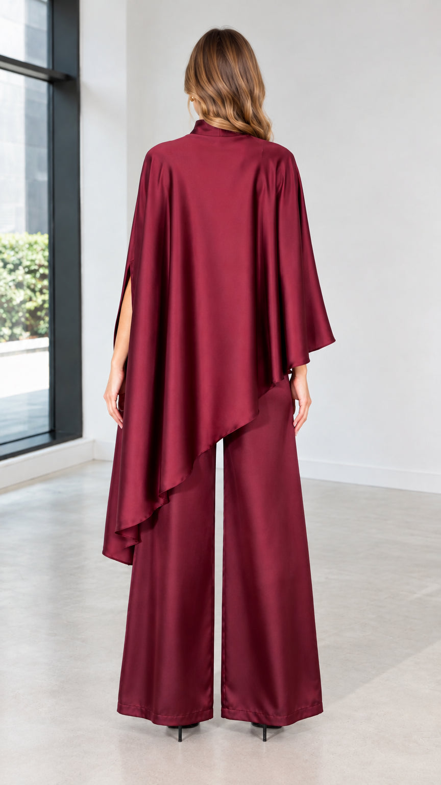 Back view of burgundy satin asymmetric cape drape and wide-leg pants coordinate