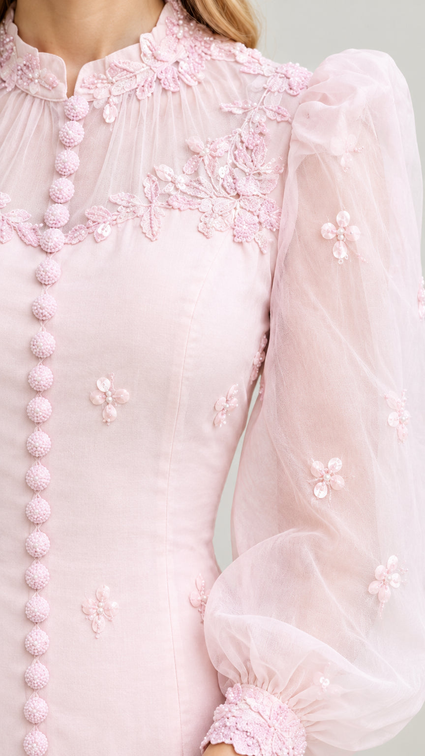 Close-up detail of blush pink sheer illusion neckline, floral lace appliques, and button accents