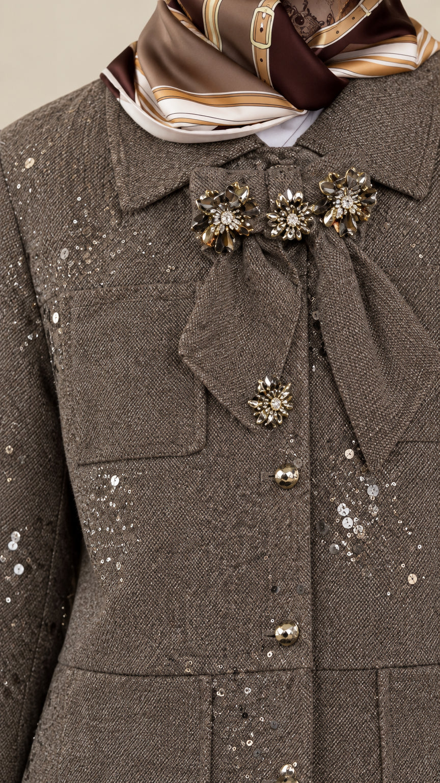 Close-up detail of jeweled brooch pins, dome buttons, and sequin fabric on taupe jacket