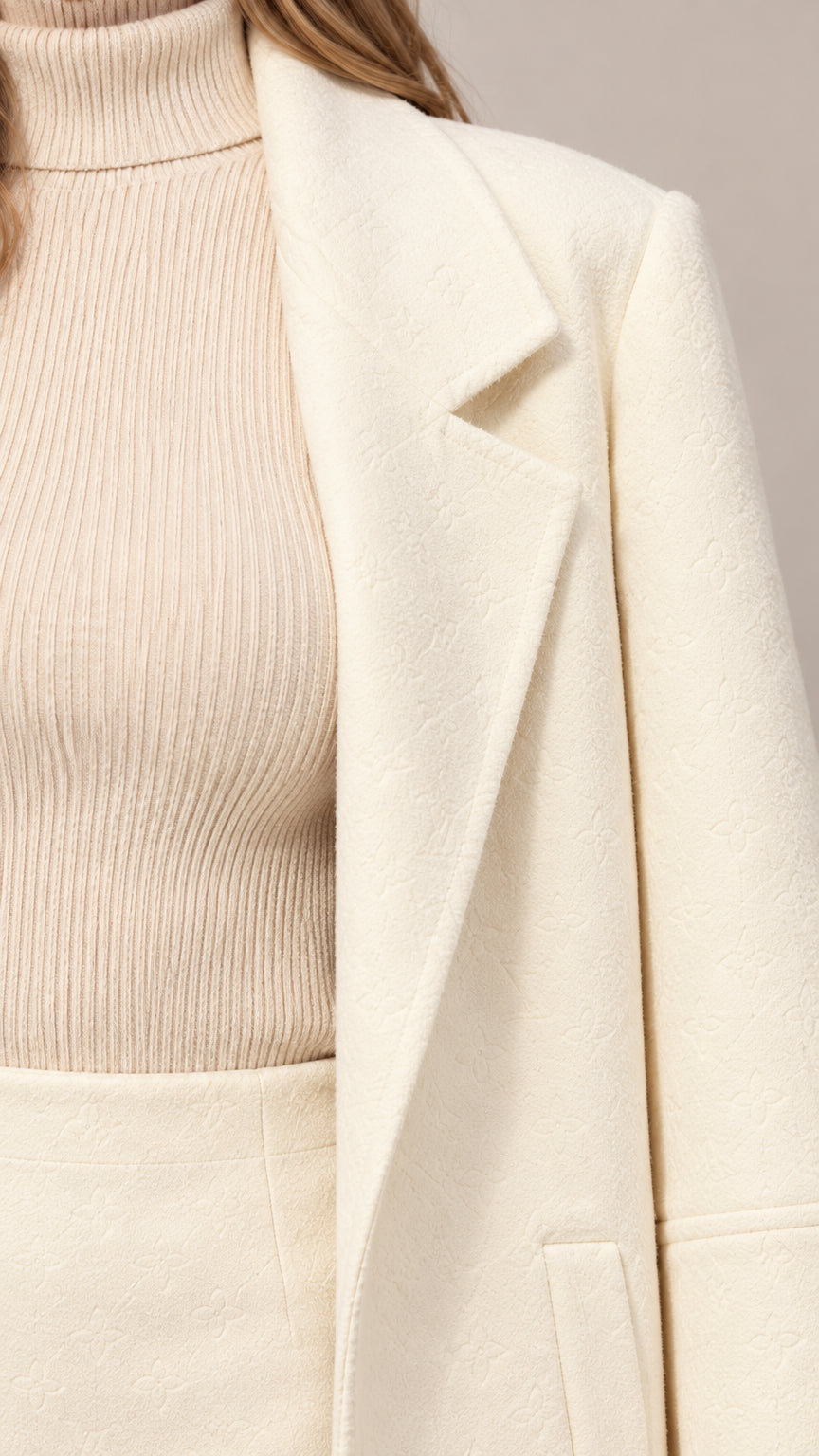 Close-up detail of cream lapel collar, ribbed mock-neck knit top, and fabric texture