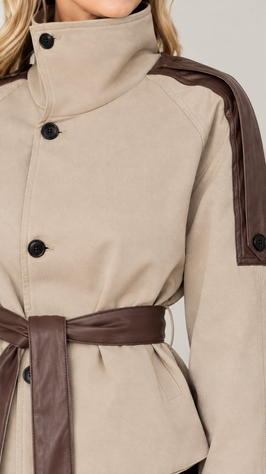 Close-up detail of high collar, buttons, and contrast shoulder patch on beige short jacket