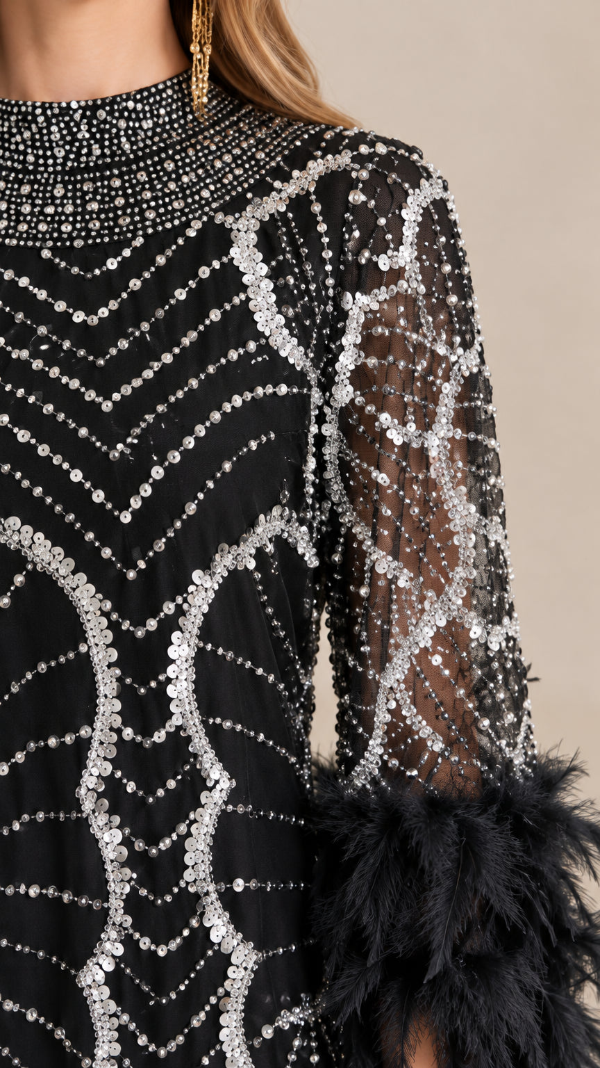 Close-up detail of silver sequin patterns, beaded neckline, and black feather cuffs