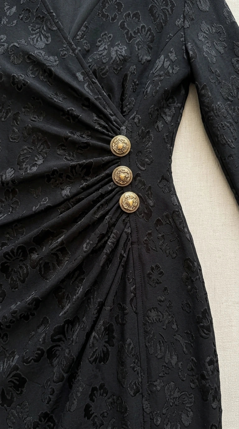 Close-up detail of black floral jacquard fabric with gathered ruching and three ornate gold buttons