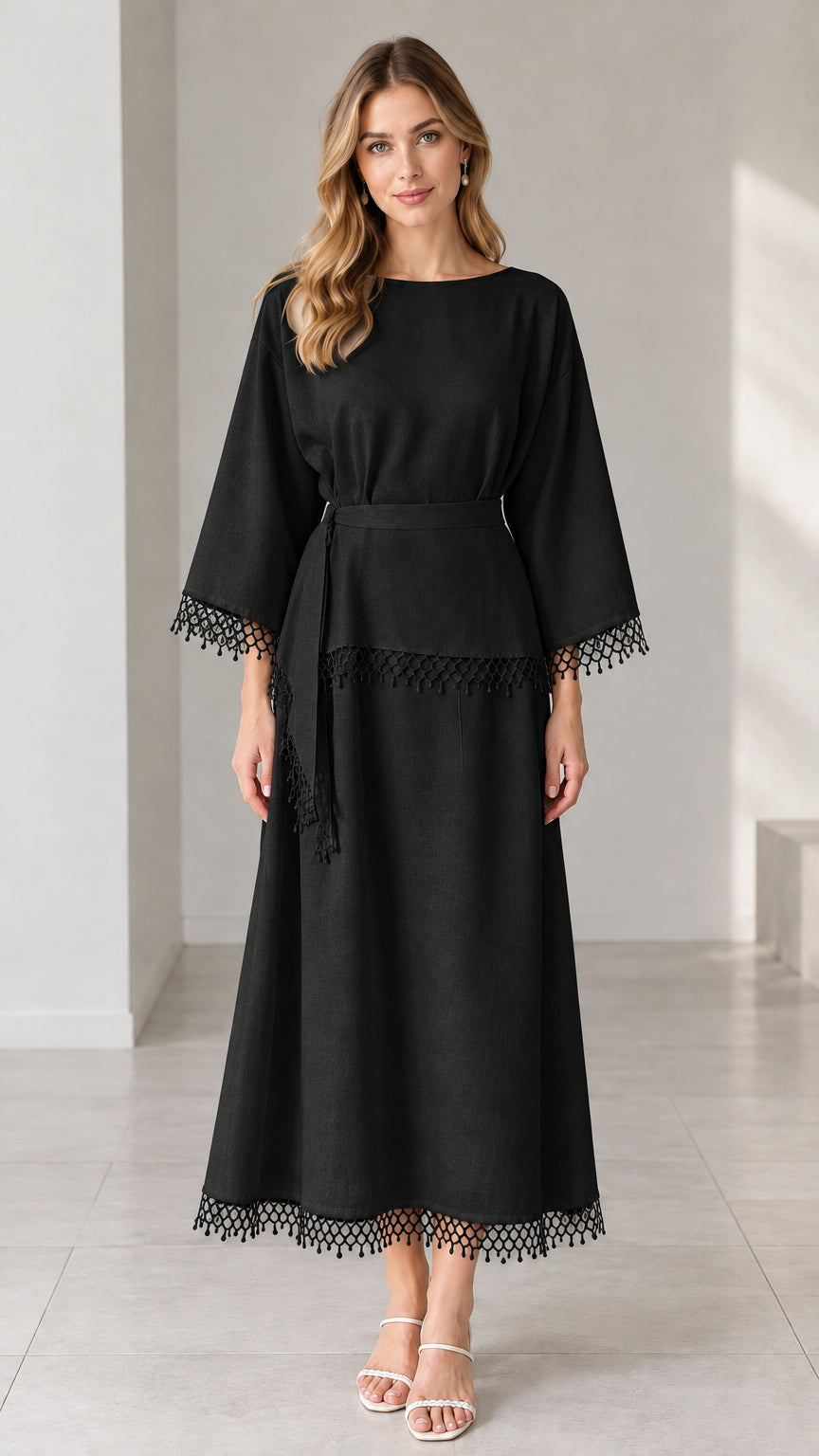 Full-length studio view of woman wearing black crochet trim belted maxi dress