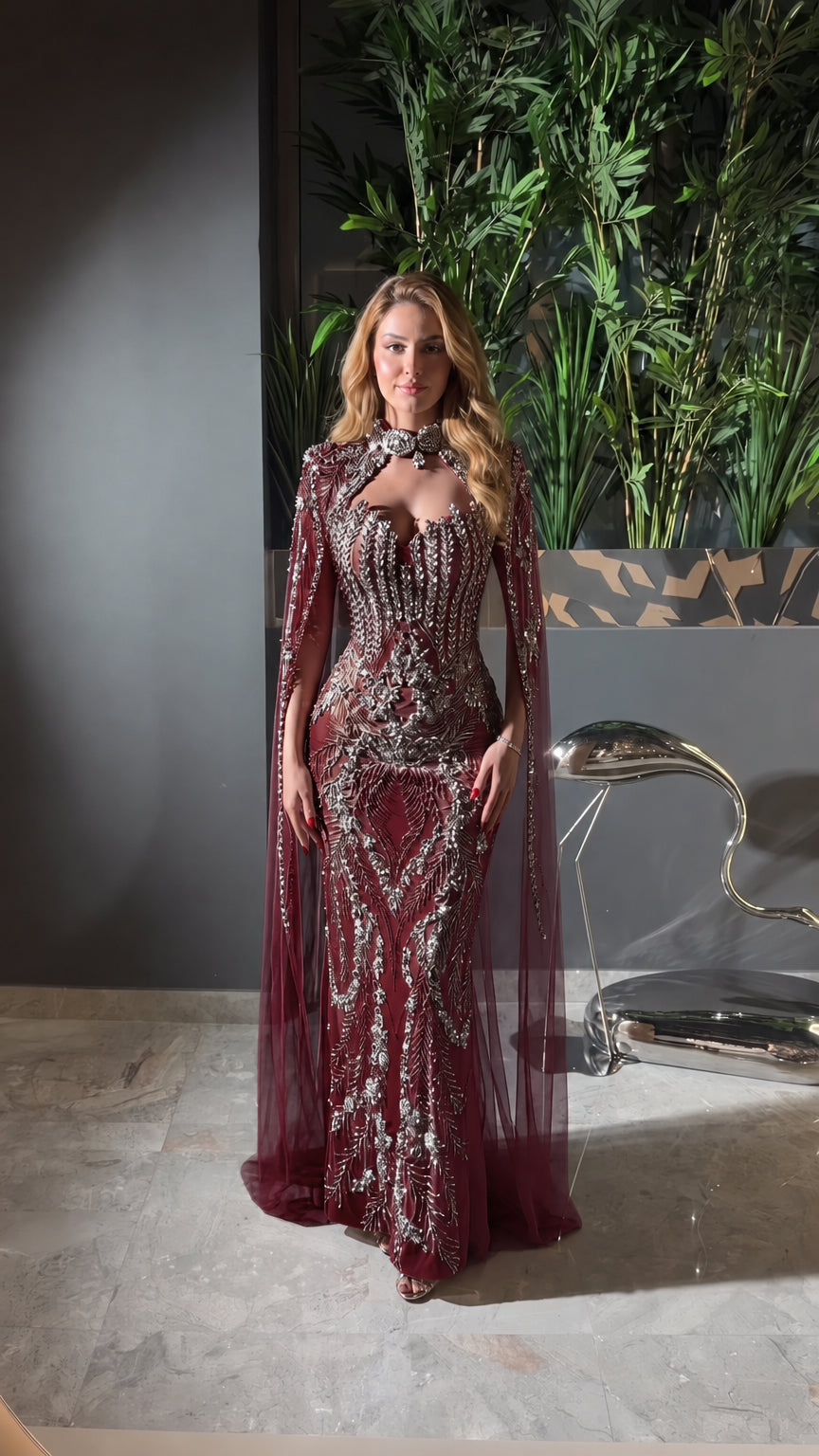 Front view of burgundy red embellished formal gown with sheer cape